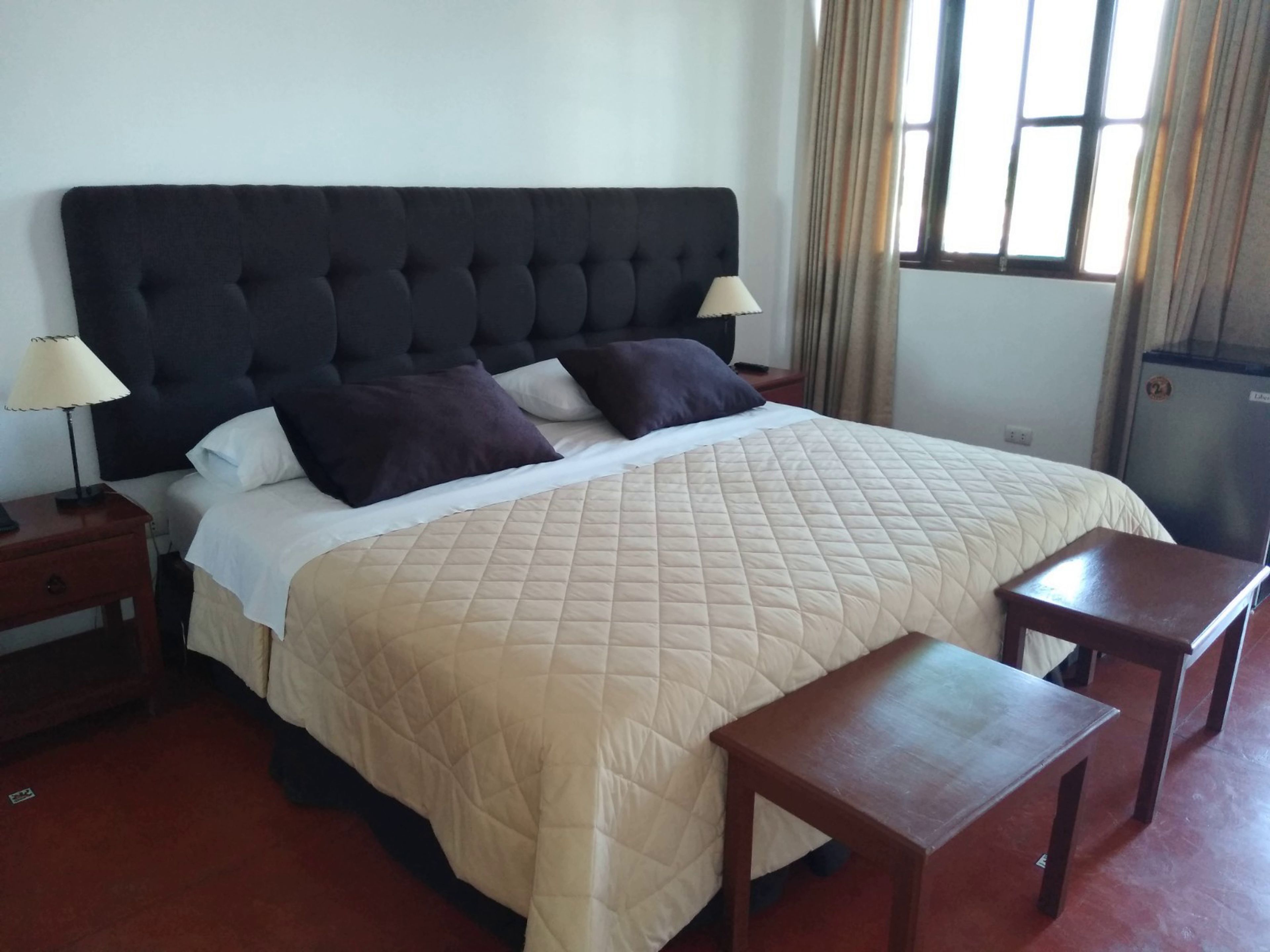 Una habitación de hotel con una cama grande, dos mesitas de noche, una lámpara y una ventana con cortinas.