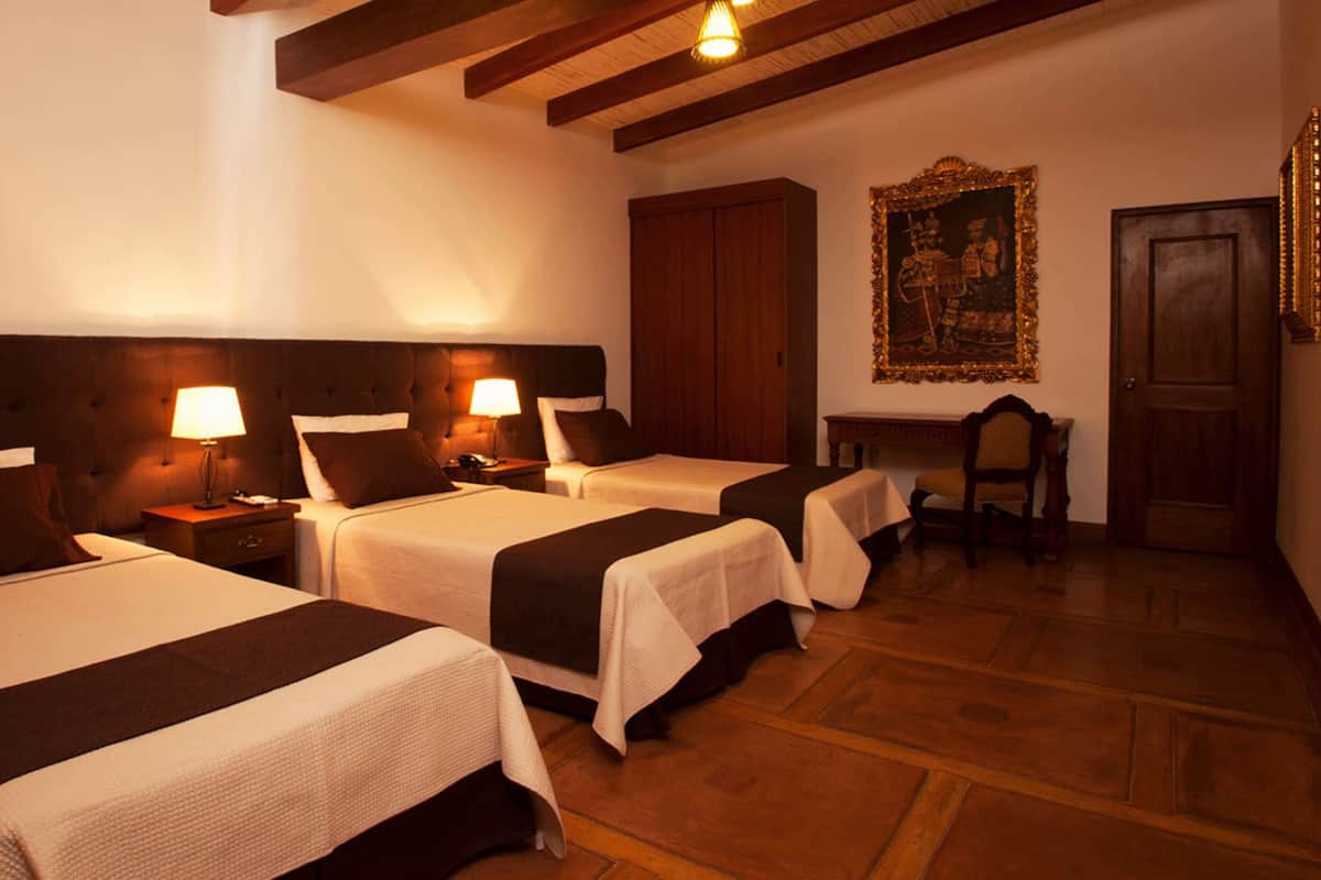 Habitación de hotel con tres camas, cabeceros de madera y un cuadro grande enmarcado en la pared.