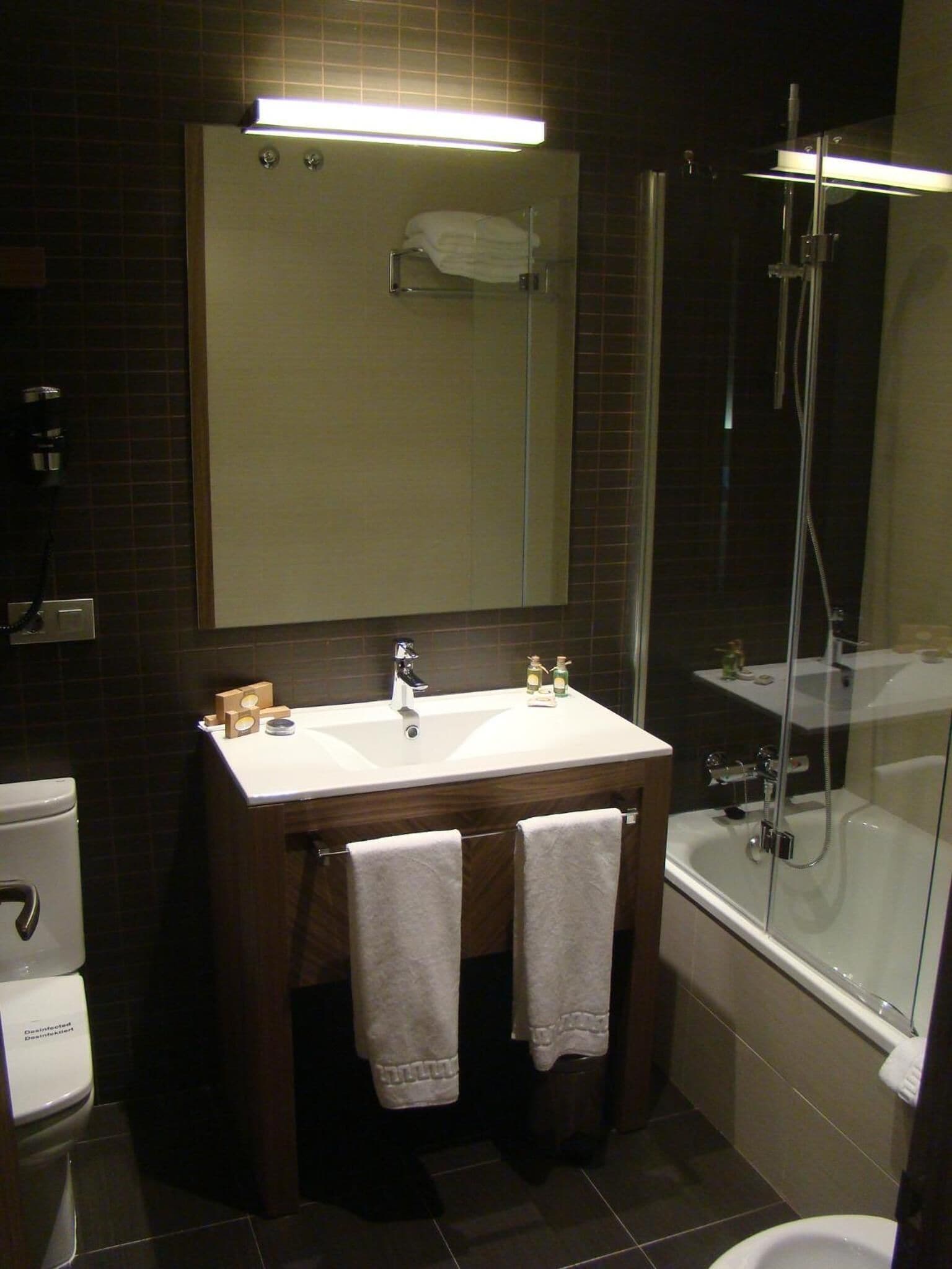 A modern bathroom with a white sink, a mirror, a glass-enclosed shower, and a toilet.