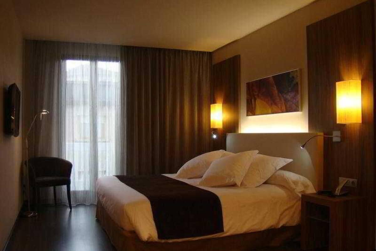 A hotel room with a large bed, a chair, a desk, and a painting on the wall.