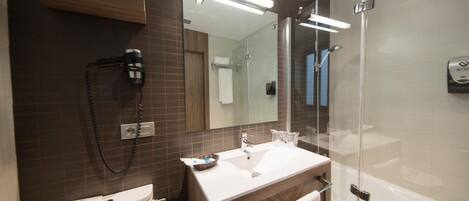 Un baño moderno con un lavamanos blanco, un espejo, una ducha y un secador de pelo.