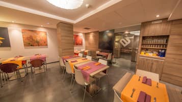 Un interior de restaurante moderno con varias mesas, sillas y una cocina visible a través de puertas de cristal.