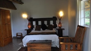 A bedroom with a wooden bed, two bedside lamps, a wooden chair, and a small table. - Matumi Game Lodge (Hoedspruit)