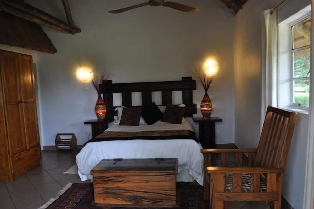 A bedroom with a wooden bed, two bedside lamps, a wooden chair, and a small table.