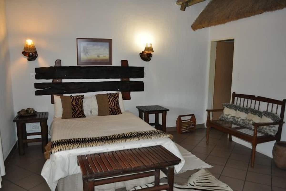 A bedroom with a wooden bed, two bedside tables, a bench, a chair, and two wall-mounted lamps.