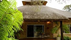 A thatched-roof building with a brick exterior, large sliding glass doors, and a patio area with a table and chairs. - Matumi Game Lodge (Hoedspruit)