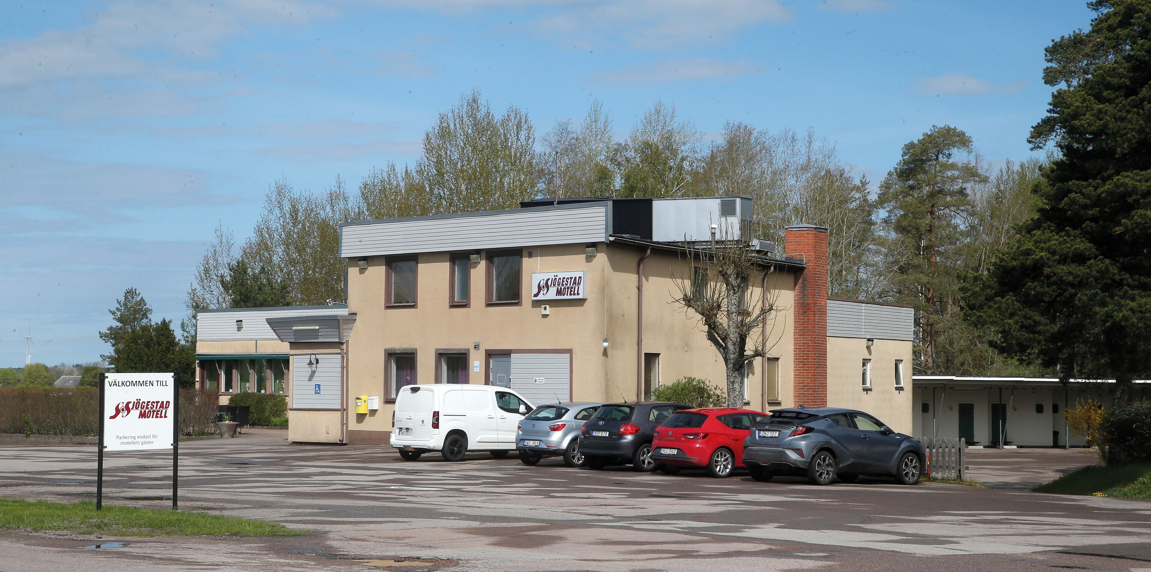 A motel with a parking lot, several cars, and a sign indicating parking availability.