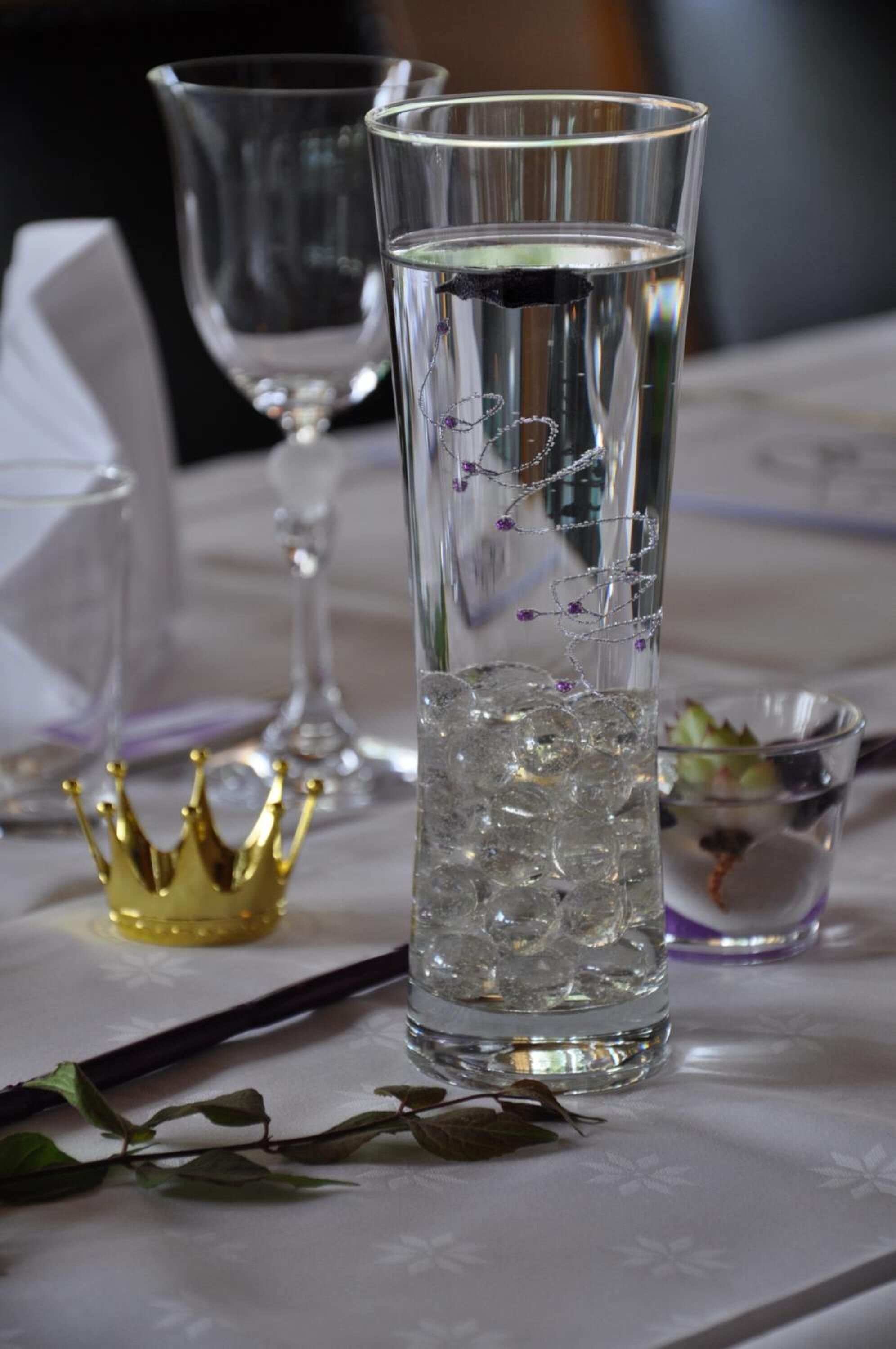 A tall glass filled with ice cubes and water, placed on a table with a white tablecloth.