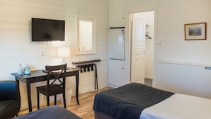 Habitación de hotel con dos camas, un escritorio con silla, televisor, refrigerador y puerta que da a un baño.