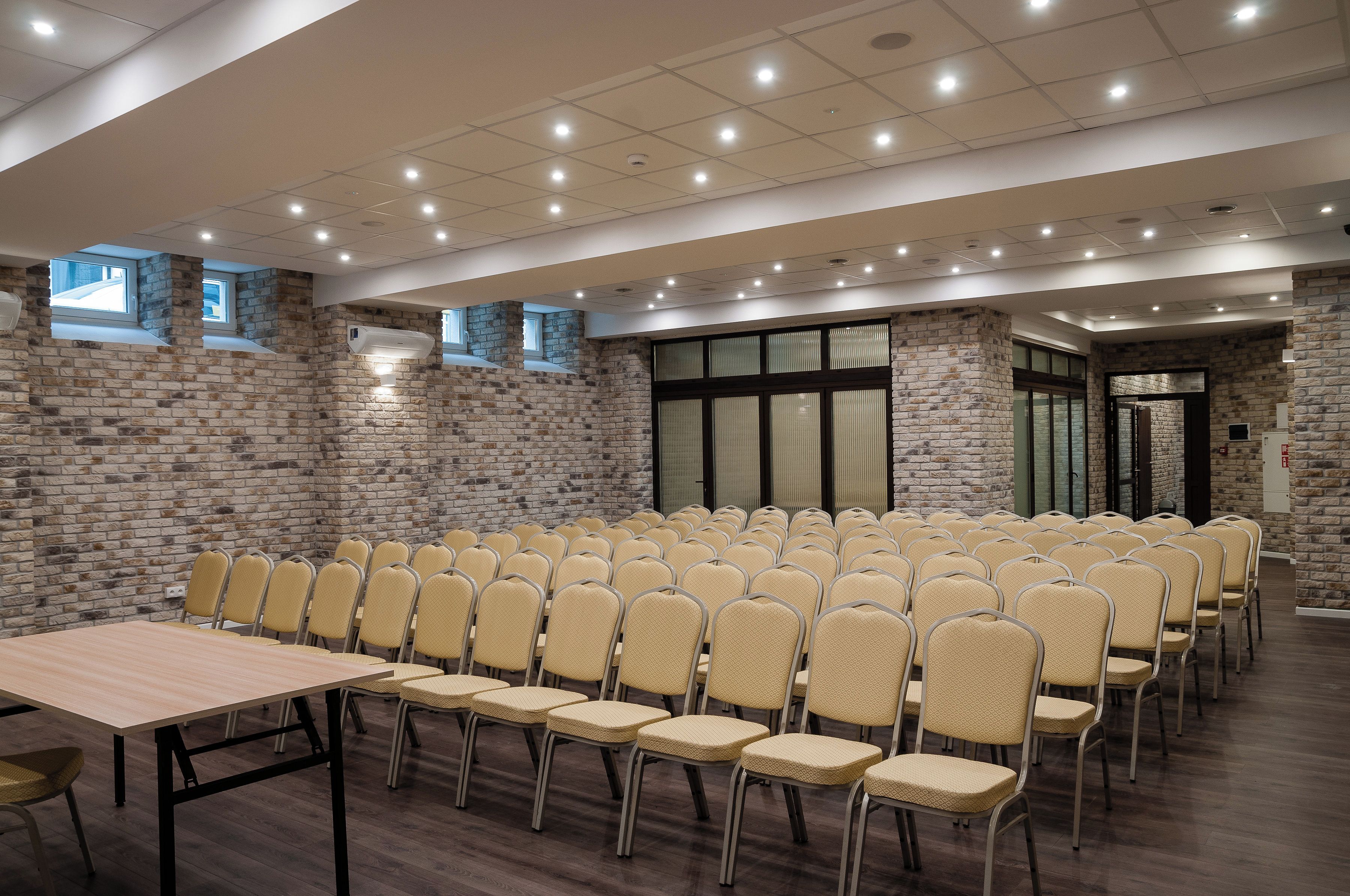 Una sala conferenze con file di sedie e tavoli, pareti in pietra e un soffitto alto con illuminazione a incasso.
