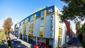 Un hotel con un llamativo letrero que dice 'HOTEL VIGA', una fachada moderna con detalles en amarillo y un estacionamiento con varios automóviles.