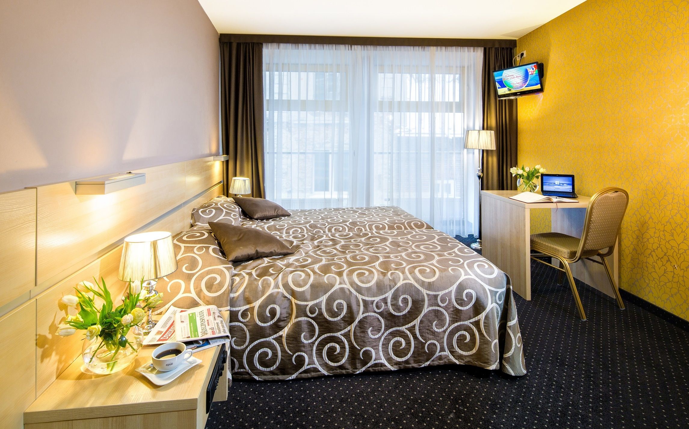 Et hotelværelse med en stor seng, et skrivebord med en computer, et fjernsyn og en stol.