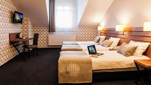 Habitación de hotel con cama, dos mesitas de noche, un escritorio con silla, televisor y ventana con cortinas.