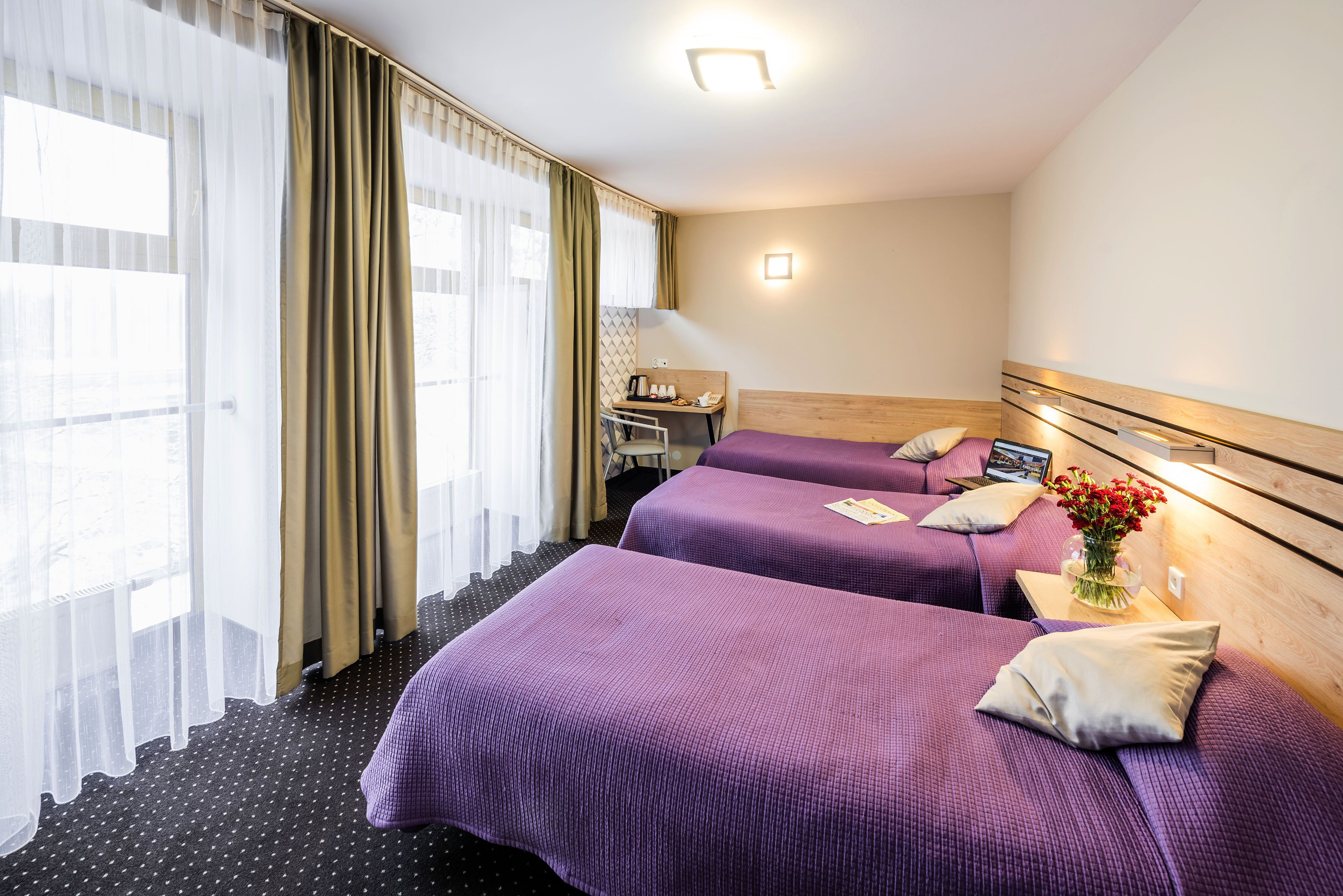 A hotel room with two beds, a desk, and a window with curtains.