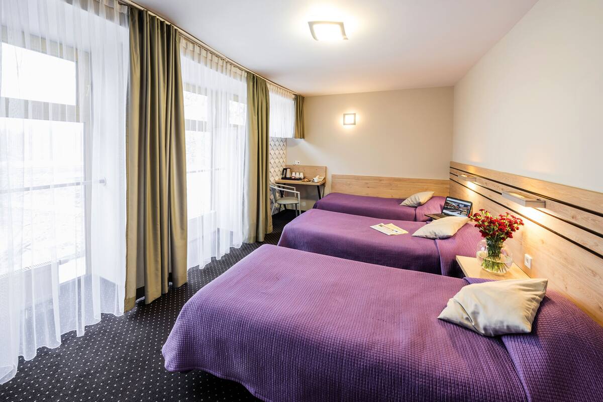 A hotel room with two beds, a desk, and a window with curtains.