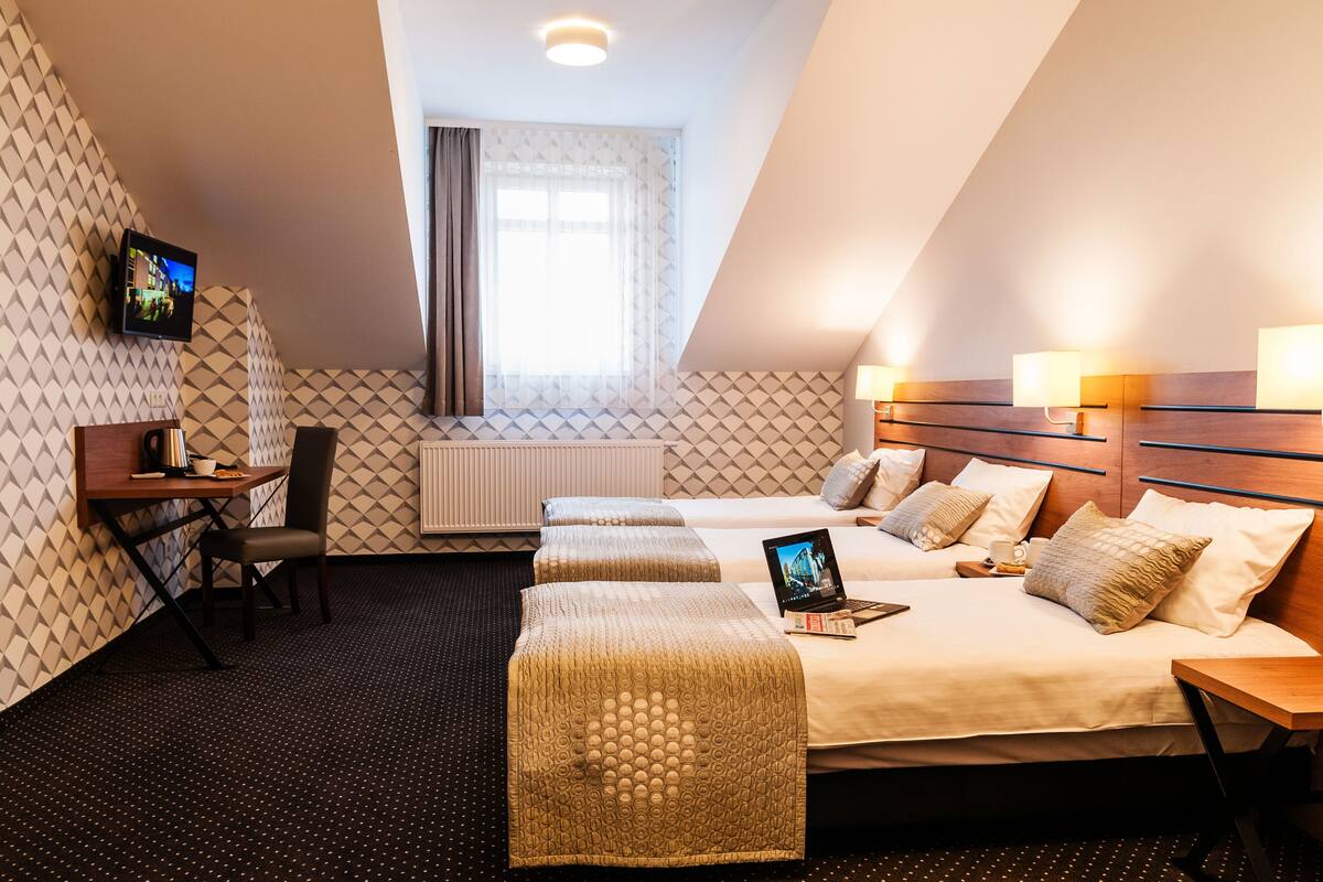 A hotel room with a bed, two bedside tables, a desk with a chair, a television, and a window with curtains.