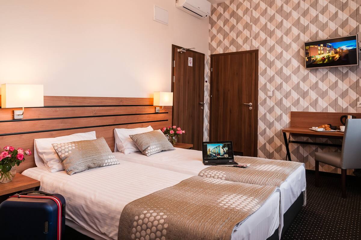 A hotel room with two beds, a desk, a TV, and a suitcase.