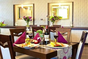 A dining table set with plates of food, wine glasses, and a bottle of wine. - Hotel Wilga (Kraków)
