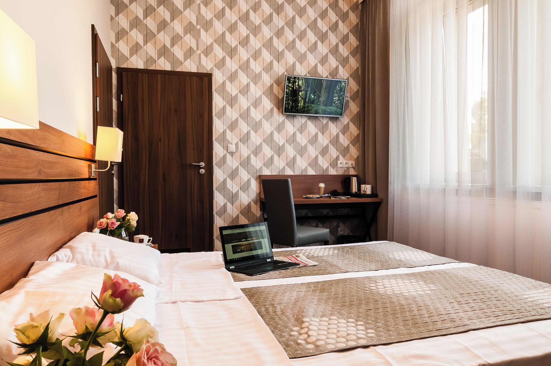 Een hotelkamer met een bed, een bureau, een laptop en een televisie aan de muur.
