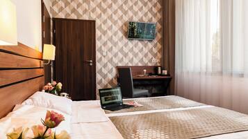 Een hotelkamer met een bed, een bureau, een laptop en een televisie aan de muur.