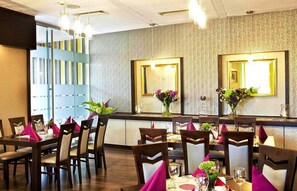 A restaurant with a modern interior, featuring a bar area with a patterned wall and mirrored panels, wooden tables with chairs, and floral centerpieces. - Hotel Wilga (Kraków)