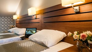 Quarto de hotel com duas camas, um laptop sobre uma delas e um vaso de flores na mesinha de cabeceira.