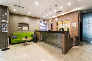 Een receptiegedeelte met een groene bank, een houten receptiebalie en een bord met de tekst 'Recepcja'.