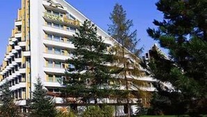 Hotel de vários andares com design moderno, com varandas e um jardim bem cuidado com árvores e arbustos.