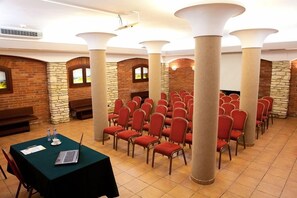 A conference room with rows of chairs, a table with a laptop, and a brick wall with arched windows. - Hotel Wilga (Kraków)