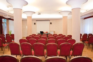 A conference room with rows of red chairs, a projector screen, and a presentation table. - Hotel Wilga (Kraków)