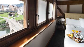 A hotel room with a bed, a tray of breakfast, a nightstand, a lamp, and a window with a view of a bridge and buildings.