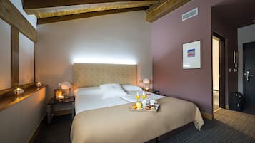 A hotel room with a large bed, a headboard, bedside tables with lamps, a framed picture on the wall, and a tray of breakfast items.