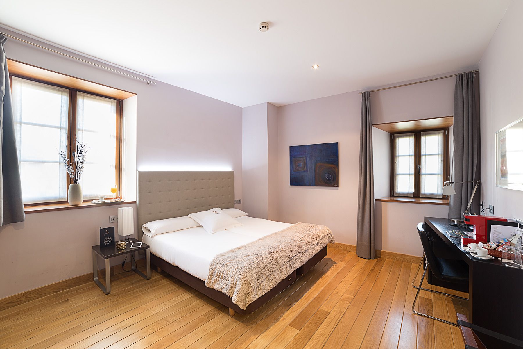A hotel room with a bed, bedside table, lamp, and a desk with a chair.