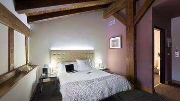 Een hotelkamer met een groot bed, houten balken, een nachtkastje met lamp en een deur naar een badkamer.