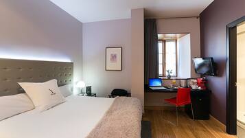 A hotel room with a bed, a desk with a laptop, a TV, and a red chair.