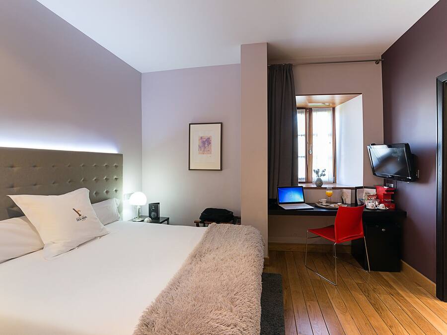 A hotel room with a bed, a desk with a laptop, a TV, and a red chair.
