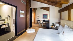 Habitación de hotel con una cama grande, un escritorio con silla, baño con lavabo y espejo, y techo de madera.