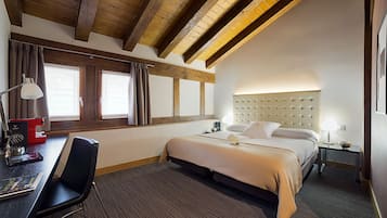 A hotel room with a bed, a desk with a chair, a lamp, and a window with curtains.