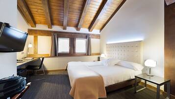 Una habitación de hotel con cama, escritorio, silla, televisión y ventana con cortinas.