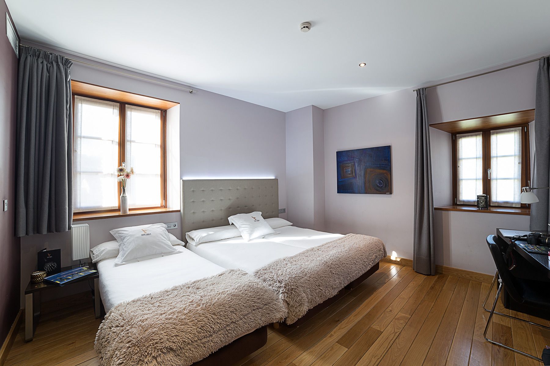 Una habitación de hotel con dos camas, un escritorio, una silla, un radiador y un cuadro en la pared.