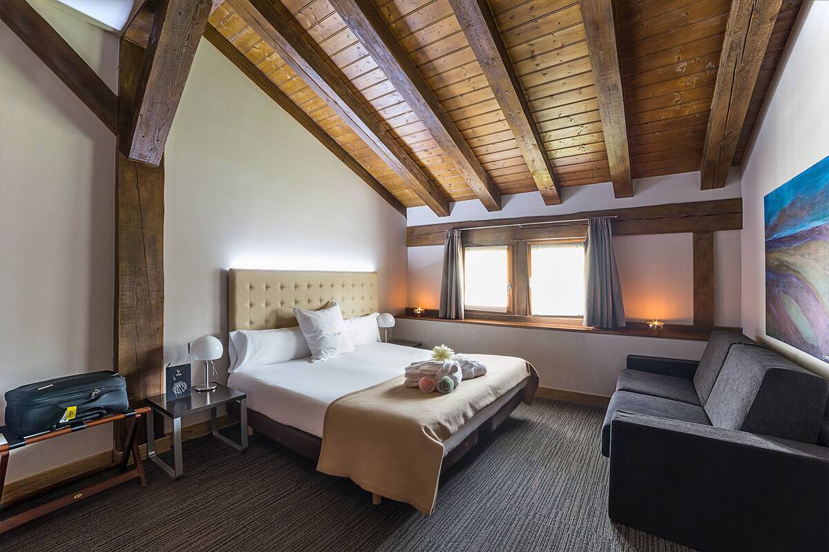A bedroom with a large bed, a desk, a chair, and a window with curtains.