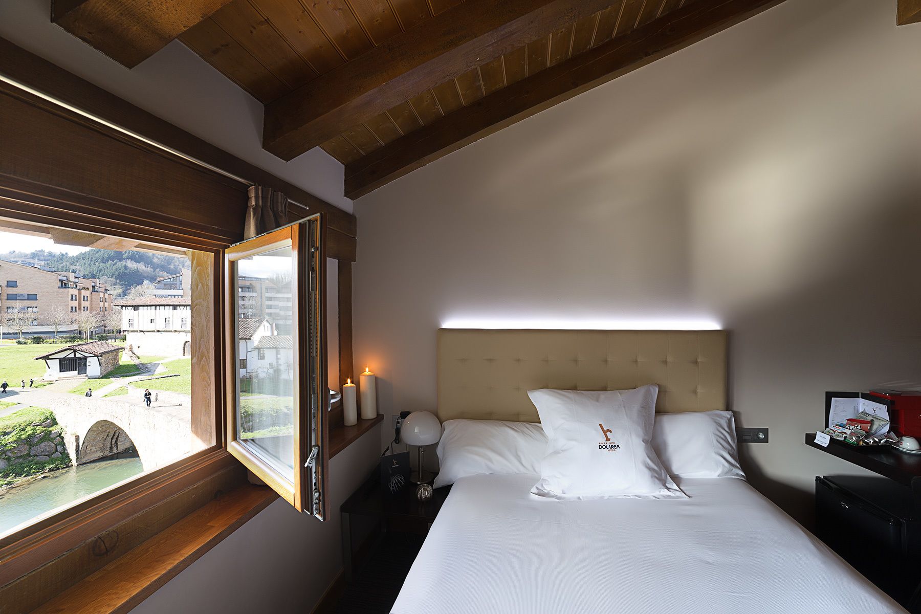 A hotel room with a bed, a nightstand, a lamp, and a window with a view of a bridge and buildings.