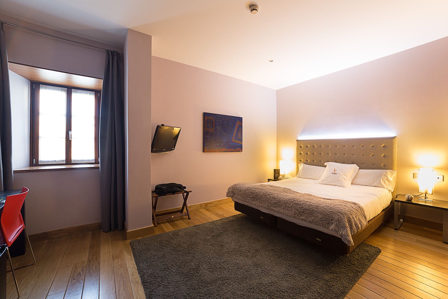 Une chambre à coucher avec un lit, des lampes de chevet, une petite table, une chaise et un tableau au mur.