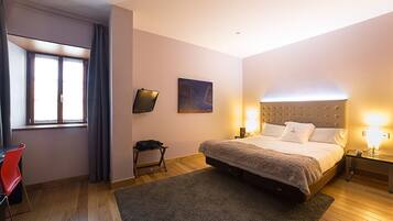 Een slaapkamer met een bed, bedlampjes, een tafeltje, een stoel en een schilderij aan de muur.
