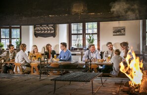 A group of people seated around tables in a rustic indoor setting with wooden benches and a visible fire.