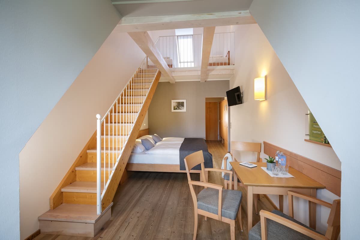 Een slaapkamer in loftstijl met een houten trap, een bed, een bureau en een stoel.