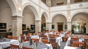 A spacious indoor dining area with multiple tables and chairs, stone columns, and a clock on the wall.