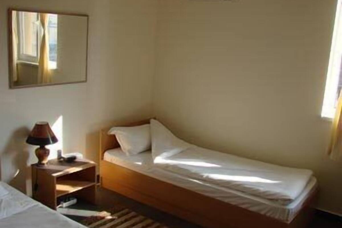 Una cama individual con estructura de madera y ropa de cama blanca en una habitación con una mesita de noche y una lámpara.