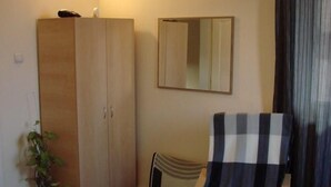 Quarto de hotel com cama, poltrona xadrez, televisão fixada na parede, guarda-roupa, espelho e planta em vaso.