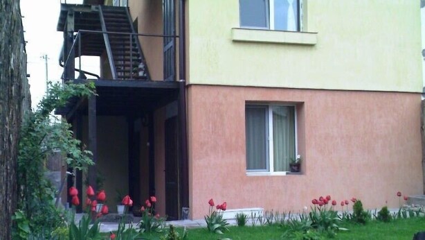 Um edifício de dois andares com varanda e um pequeno jardim com tulipas vermelhas.